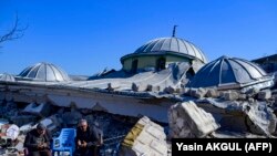 Местные жители сидят рядом с развалинами разрушенной мечети в Хатае, 10 февраля 2023 года, после землетрясения магнитудой 7,8, в результате которого погибло более 34000 человек.