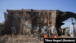 Stanovnici i milicije stoje pored kuća uništenih u zračnom napadu tokom borbe između Etiopskih nacionalnih odbrambenih snaga (ENDF) i snaga Narodnog oslobodilačkog fronta Tigraj (TPLF) u gradu Kasagita, regija Afar, Etiopija, 25. februara 2022.
