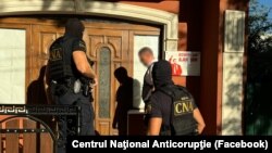 CNA precizează că în urma perchezițiilor „au fost ridicate sume de bani, în lei și valută, purtători de informații și zeci de carduri bancare”.