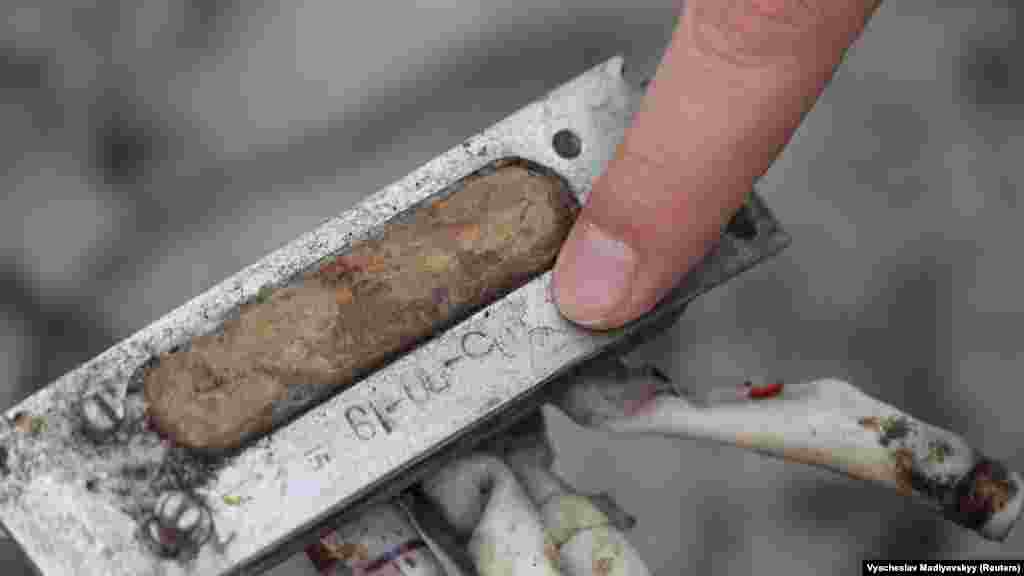 Dmitro Csubenko, a harkivi ügyészség munkatársa rámutat egy rakétatöredékről származó írásra, amely sem cirill, sem latin betűsnek nem tűnik