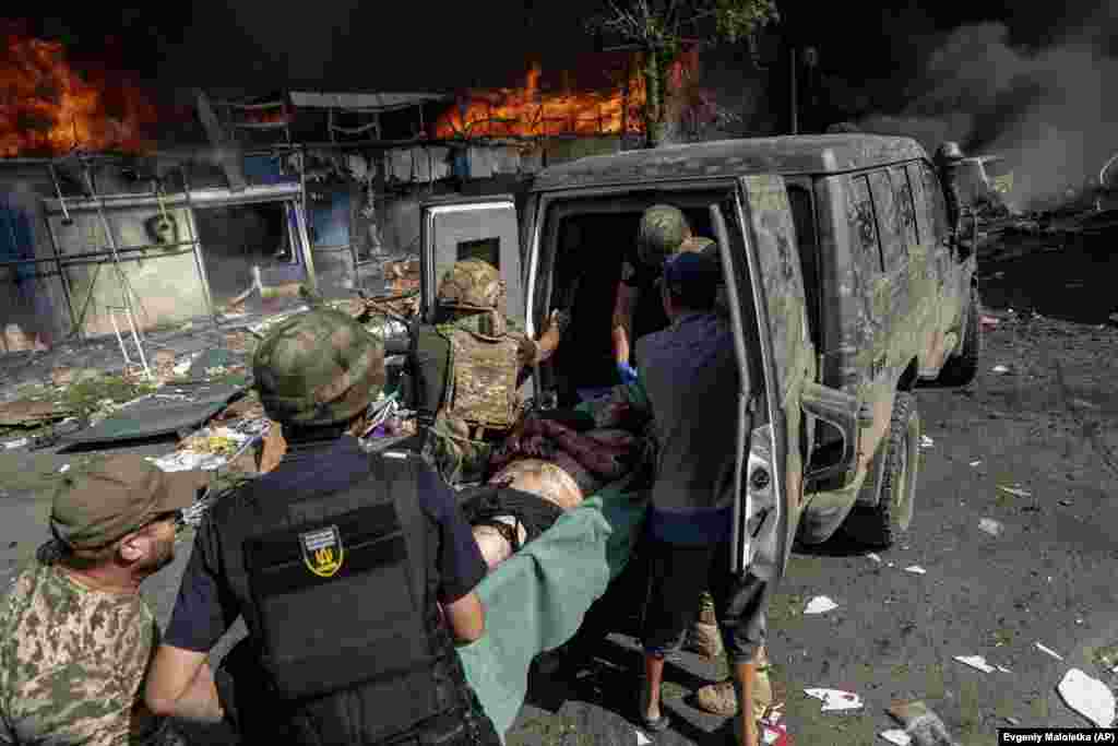 An injured man is carried into an ambulance as fires burn in the background.
