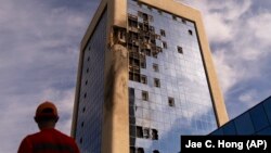 Egy karbantartó munkás áll egy dróntámadásban megrongálódott kormányzati épület előtt Kijevben 2023. augusztus 2-án