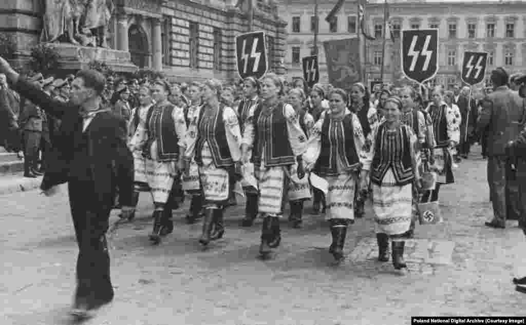 Gratë ukrainase me veshje tradicionale duke kaluar nën banderola naziste në Lviv gjatë një vizite zyrtare nga Hans Frank, udhëheqësi gjerman i Polonisë së pushtuar nga nazistët. Shumë nacionalistë ukrainas patën qëndrimin &quot;armiku i armikut tim është miku im&quot; ndaj pushtimit nazist, duke u dhënë meritën gjermanëve për dëbimin e bolshevikëve komunistë. Disa ukrainas morën pjesë aktive në vrasjet masive të hebrenjve, ndërsa të tjerë, &quot;individë dhe nganjëherë fshatra të tëra&quot;, rrezikuan gjithçka për të strehuar hebrenjtë nga nazistët.