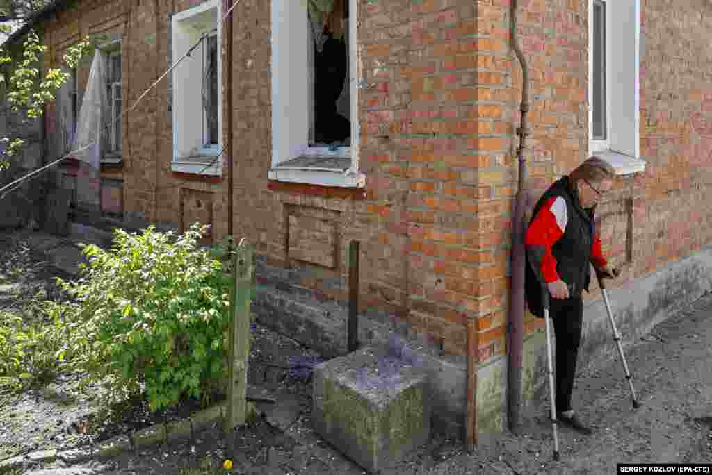 Жена со хендикеп одмора пред нејзиниот оштетен дом по гранатирањето во Харков, Украина.