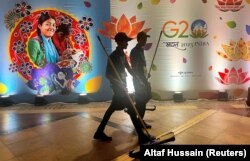 Прибиральники проходять повз рекламу в Міжнародному медіа-центрі під час саміту G20 у Нью-Делі, Індія, 9 вересня 2023 року