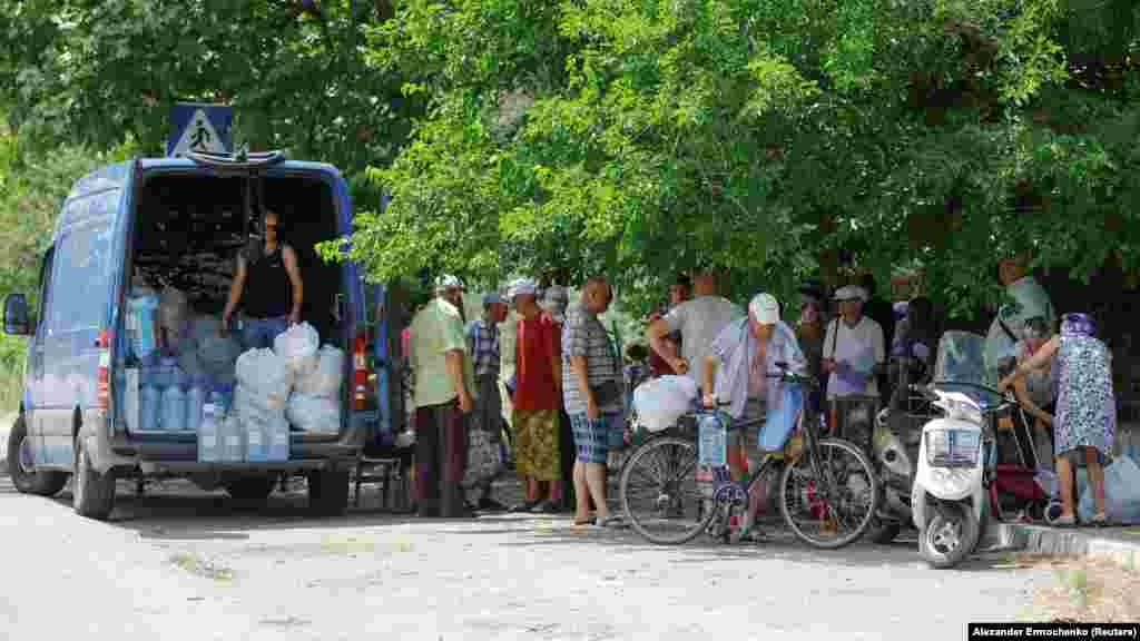 Helyiek ivóvízért és élelmiszerért állnak sorba Hola Prisztanban 2023. július 6-án.&nbsp;A hatezer lelkes települést több mint egy hónapja, a kahovkai gát felrobbantását követő napon árasztotta el a víz. Az orosz ellenőrzés alatt álló területen akkor karantént hirdettek, ezért mind az evakuálás, mind a segélyszállítmányok eljuttatása akadályokba ütközött