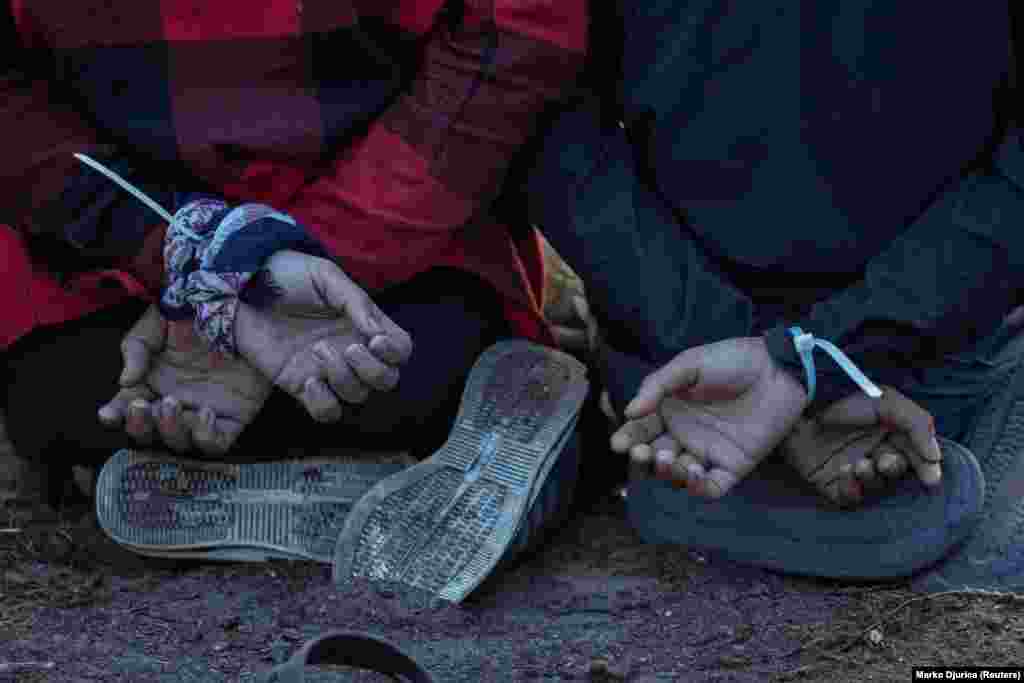 Pritvoreni migranti sjede na koljenima s rukama vezanim lisicama u blizini svog improviziranog kampa blizu granice. &quot;Onda ovi pojedinci ponovo padaju u kandže krijumčara koji ponovo traže plaćanje&quot;, rekao je on, dodajući da su različite kriminalne grupe bile uključene u krijumčarenje migranata i međusobno nasilje.