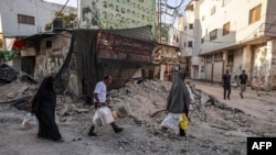 Ljudi nose kese sa humanitarnom pomoći dok hodaju među ruševinama nakon vojne operacije u izbjegličkom kampu Dženin na okupiranoj Zapadnoj obali, 5. juli