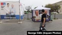 Un bărbat din București trece pe lângă două bannere care prezintă candidați la Primăria Generală, respectiv de sector din București