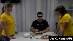 Denisz Abdulin, a háborúban megvakult egykori ukrán katona oktatókkal tanulja a konyhakés használatát egy rehabilitációs központban tartott főzőtanfolyamon