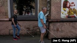 Olekszandr Zsilcsenko (jobbra) és Ivan Szoroka, két volt ukrán katona, aki a háborúban megvakult, botjukkal az ukrajnai Rivne utcáin 2023. július 21-én