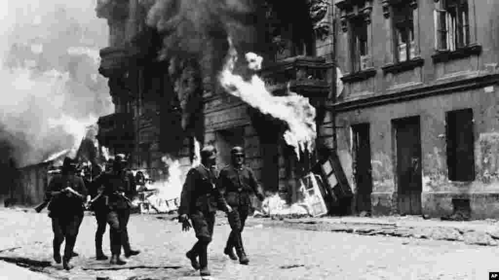 След потушаването на въстанието на 16 май 1943 г. нацистките войници взривяват синагогата. Този кадър е уловил как нацистки офицери се разхождат по улиците, докато сгради във Варшавското гето горят.&nbsp;