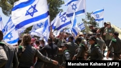 Демонстранттар Кнессеттин жанында Израилдин желегин кармап турушат.