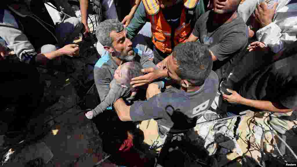 Palesztinok viszik egy gyermek holttestét, amelyet egy izraeli csapás által eltalált családi ház romjai alól emeltek ki a Gázai övezet középső részén lévő Nuszejratban 2024. május 14-én