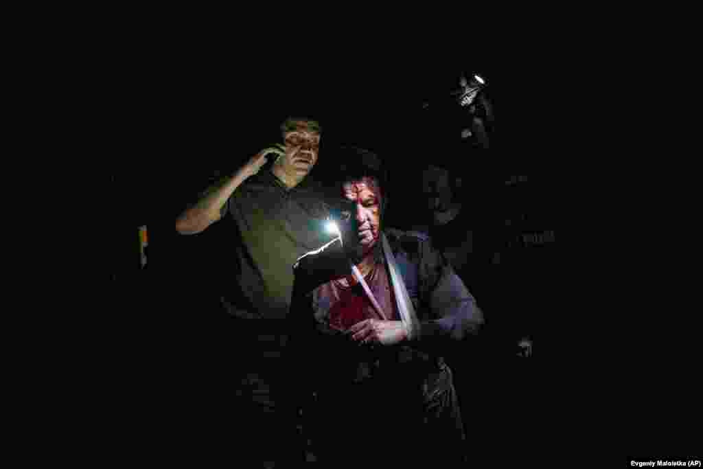 Ukrajinski policajac razgovara na telefonu, nakon što je učestvovao u pružanju pomoći Nataši, jednoj od ranjenih u ruskom raketnom napadu, u noći 21. juna. Sa tragovima krvi na licu, i previjenom rukom, sada čekaju hitnu pomoć.&nbsp;