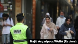 Egy iráni rendőr áll az utcán az erkölcsrendészet újraindítása után Teheránban 2023. július 16-án. A képen szereplő egyik nő nem visel kendőt