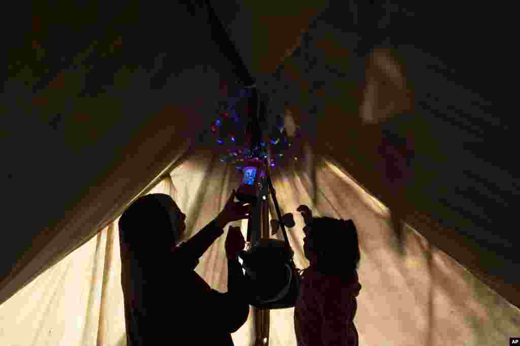 Ранда Бејкер, која е раселена поради израелското бомбардирање на Појасот Газа, закачува рамазански украси и лампиони со својата ќерка, одбележувајќи го почетокот на месецот Рамазан, во импровизиран шаторски камп во областа Муваси, во јужниот дел на Појасот Газа, март 11. &bdquo;Почетокот на Рамазан беше тажен и покриен во темнина, со вкус и мирис на крв насекаде. Израелската окупација не сака да имаме никаква радост за време на Рамазан. Немаме храна за нашата трпеза за ифтар&ldquo;, изјави раселени Палестинец, 50- годишниот Ауни ал Кајјал.