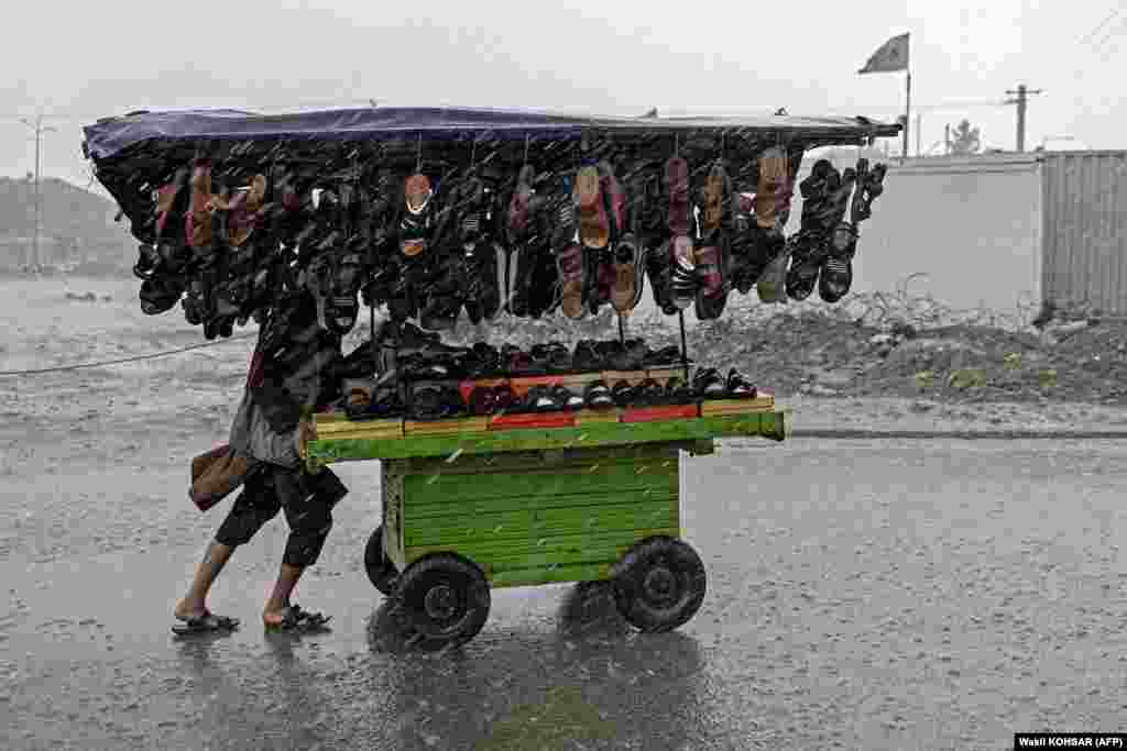 Afganistanski prodavac gura kolica puna obuće kroz ulicu dok pada kiša u Kabulu.