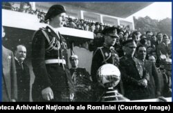 1934. Principele moştenitor Mihai, la un meci de fotbal. În fața sa, un trofeu în forma unei mingi de fotbal.