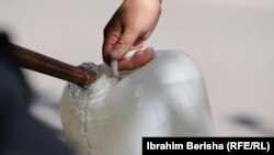 Një person duke mbushur në bidon me ujë. Uji i Liqenit të Badocit nuk rekomandohet të përdoret për pije dhe gatim.