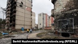 Жители на фоне фрески британского художника Бэнкси на обугленном фасаде жилого дома в Ирпене — городе недалеко от Киева, который сильно пострадал во время российского вторжения и оккупации, апрель. Автор: Сергей Нужненко, украинская редакция «Азаттыка».