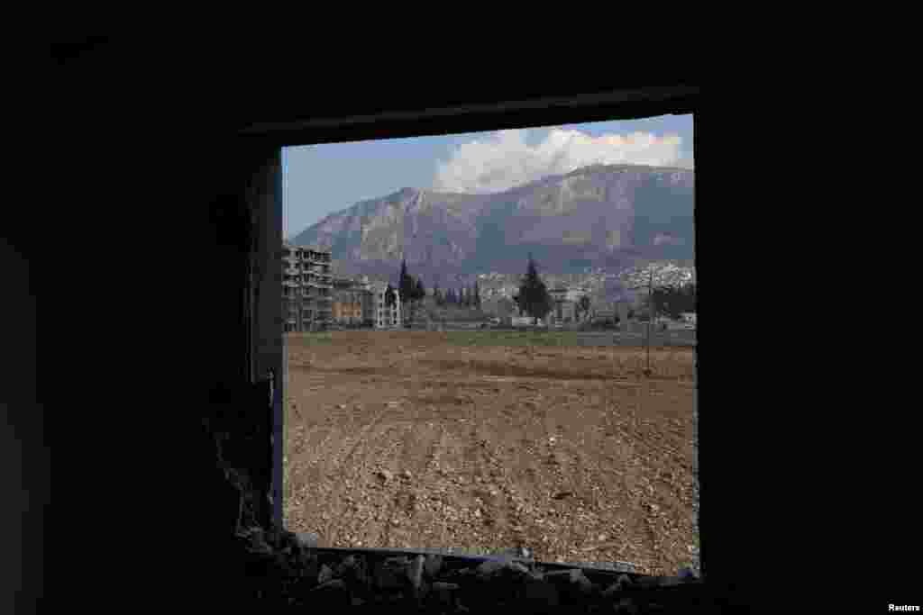 Një vend tashmë i pastruar ku kishte ndërtesa para tërmetit të vitit të kaluar, shihet përmes dritares së një ndërtese të dëmtuar në Hataj, Turqi, shkurt 2024.