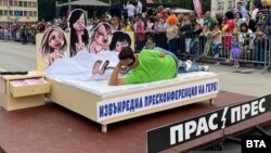 Карикатури на жени от преговорния екип на ГЕРБ за съставяне на ротационно правителство са поставени в легло, от което дават пресконференция на ГЕРБ. До спалнята има нощно шкафче с чекмедже, в което се виждат банкноти. Композицията е част от карнавала в Габрово.