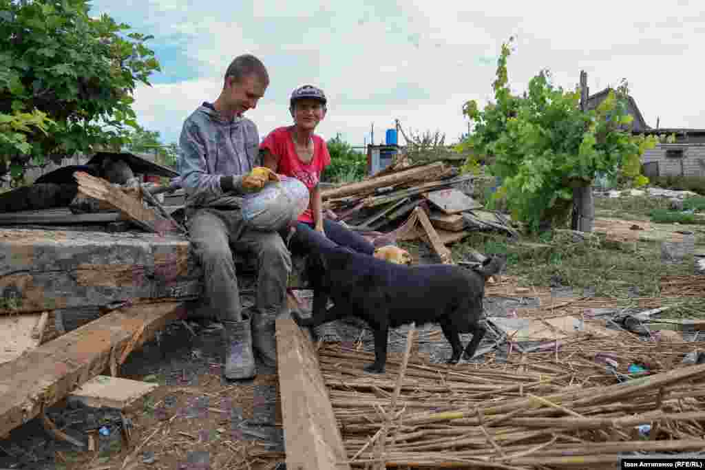 Jevhen és édesanyja, Aljona egykori házuk előtt. Otthonukat elpusztította az árvíz, ezért egy rokonuknál élnek a faluban.&nbsp;Több ezer otthont érintett a június 6-i kahovkai gátszakadás, amely elárasztotta a Dnyeper folyó mentén fekvő településeket, és Oroszország teljes körű inváziójának legnagyobb környezeti katasztrófájához vezetett