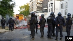 Policija u opremi za nerede čuva stražu dok vatrogasci rade na gašenju požara nakon demonstracija u Nanterreu, zapadno od Pariza, 27. juna 2023.