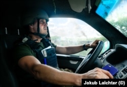 Олексій Савкевич везе гуманітарну допомогу в Авдіївку, а на задньому плані піднімається стовп диму. Фото від серпня 2023 року