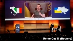 Прем’єр-міністри України та Італії – Денис Шмигаль і Джорджа Мелоні – слухають виступ президента України Володимира Зеленського (на екрані) під час Конференції з відновлення України. Рим, 26 квітня 2023 року