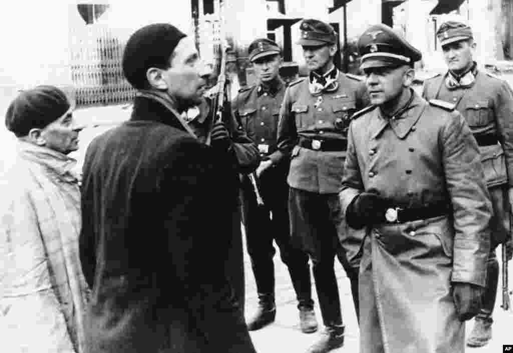 Въстанието избухва на 19 април 1943 г., за да попречи на силите на Хитлер да ликвидират Варшавското гето и да отведат останалите евреи на сигурна смърт в лагерите Треблинка, Аушвиц и Майданек. На снимката се виждат офицери от СС в гетото по време на разрушаването му през пролетта на 1943 г.