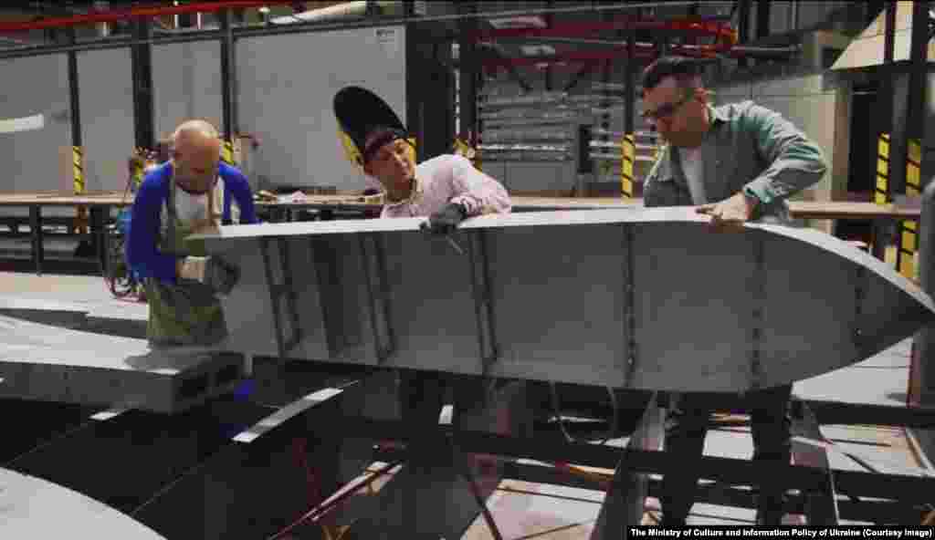 Ukrán munkások a háromágú pajzs egy részével. Az újság nem nevezte meg a helyet, ahol az új szoborelem készül. A huszonnyolc millió hrivnyás (körülbelül kétszázötven millió forint) acélpajzs finanszírozását különböző ukrán nagyvállalatok adományaiból teremtették elő &nbsp;