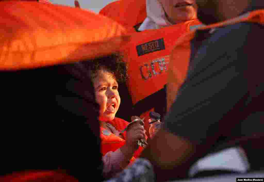 Një fëmijë shihet duke ngrënë derisa qëndron në bordin e një varke së bashku edhe me dy vajza të tjera, në pritje për t&#39;u ndihmuar nga OJQ-ja Open Arms.