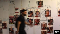 Një person kalon pranë një muri ku janë vendosur fotografitë e pengjeve izraelite të kapura nga Hamasi. Tel Aviv, 21 nëntor 2023. 