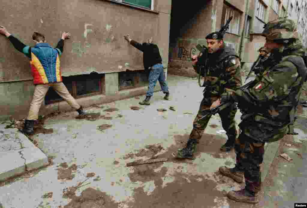 Soldați italieni păzesc presupuși piromani în Sarajevo în martie 1996. Zeci de mii de soldați NATO au fost mobilizați pentru conflictul din Bosnia. De atunci, Alianța a invocat articolul 5 împotriva Afganistanului, după atacurile teroriste din 11 septembrie 2001, și a intervenit în războiul civil din Libia.