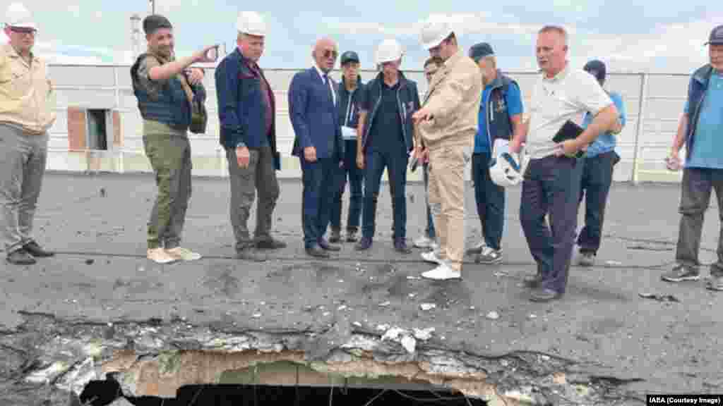 A Nemzetközi Atomenergia-ügynökség ellenőrei, köztük Rafael Grossi, a NAÜ vezetője (jobbra középen kék mellényben) egy nukleáris üzemanyagot tároló épületre csapódott gránát okozta sérüléseket vizsgálnak 2022 szeptemberében.&nbsp;Grossi és Putyin idei, március 6-i zárt ajtós találkozójának részletei nem világosak, a NAÜ vezetője csupán egy &bdquo;fontos eszmecserét&rdquo; jelentett be az atomerőművel kapcsolatban
