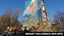 Українські військові та енергетики стоять перед муралом, присвяченому українським військам ППО та енергетикам у Києві. Україна, 30 листопада 2023 р.