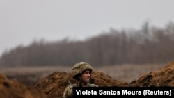 A 80. ukrán ejtőernyősdandár katonája figyeli környezetét a frontvonal egyik lövészárkából Bahmut közelében 2023. március 16-án