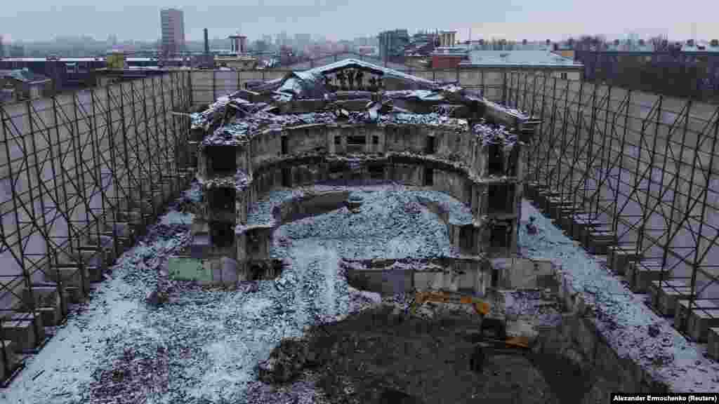 A félig lerombolt mariupoli színház, amelyet 2022. március 16-án bombáztak az orosz katonák, a jelentések szerint több száz, benne menedéket kereső civilt megölve. Ma a romos épületet magas kerítés védi, amelyet orosz írók képei díszítenek &nbsp;