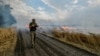 Украински военнослужещ върви сред горящо житно поле близо до фронтовата линия на границата между Запорожка и Донецка област, Украйна, на 17 юли 2022 г.