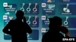 Vizitorët qëndrojnë para një ekrani që shfaq promovimim e kriptomonedhave në Tajlandë. 12 maj 2022.