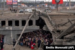 Жителі нищеного російськими військами міста Ірпінь, намагаються пішки евакуюватися під обстрілами, перетинаючи річку по уламках підірваного моста. Україна, за 20 кілометрів від Києва. 5 березня 2022 року