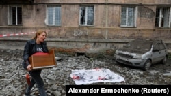 Žena prolazi pored pokrivenog tela osobe ubijene u nedavnom granatiranju u blizini oštećenog stambenog bloka u Makijevki u istočnoj Ukrajini 4. novembra