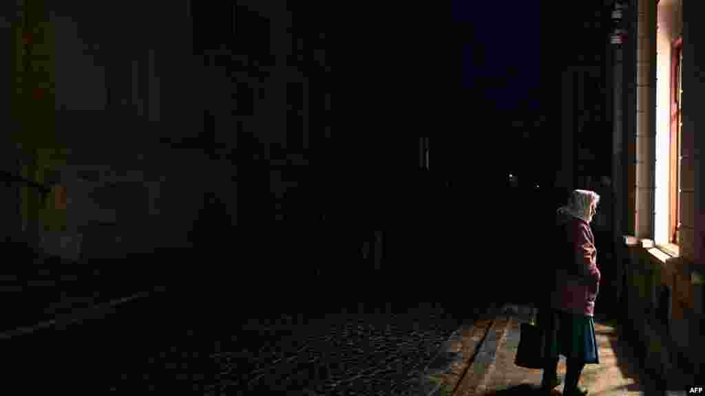 Egy idős nő bepillant egy lámpafényes ablakon az egyik vaksötét lvivi utcán