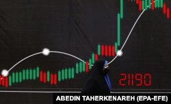 Egy nő sétál egy transzparens mellett a 26. Nemzetközi olaj-, gáz- és petrokémiai nemzetközi kiállításon Teheránban, Iránban 2022. május 13-án. Az iráni olajügyi minisztérium szerint több mint ezer vállalat vett részt a kiállításon, de sok nagy nemzetközi vállalat nem tudott megjelenni az iráni atomprogram nyomán Irán ellen hozott amerikai szankciók miatt