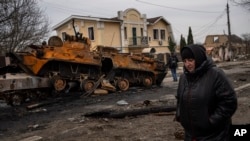 Жена минава покрай разрушена руска бронирана машина в Буча