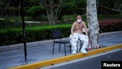 Un muncitor în costum de protecție se odihnește în fața unui centru Covid din Shanghai, 11 aprilie 2022.