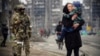 Жена со дете поминува покрај руски војници на улица во Мариупол на 12 април.