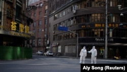 Lucrători în costume de protecție supraveghează o stradă în timpul carantinei, pe fondul pandemiei de Covid, în Shanghai, China, 16 aprilie 2022.